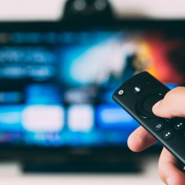 pessoa segurando controle remoto, tv exibe a tela inicial da amazon prime