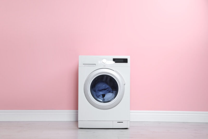 Máquina de lavar roupas em frente de parede rosa.