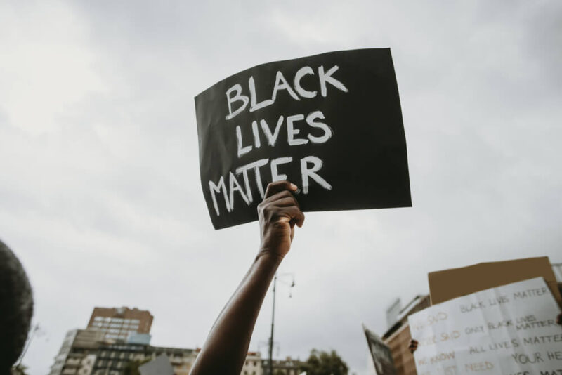 Mão segurando um cartaz escrito "black lives matter" (vidas negras importam, em inglês).