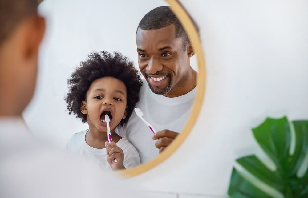 Pai e filho negros, escovando os dentes enquanto se olham em um espelho redondo