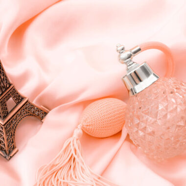 Um frasco de perfume e uma miniatura da Torre Eiffel sob um tecido de cetim rosa.