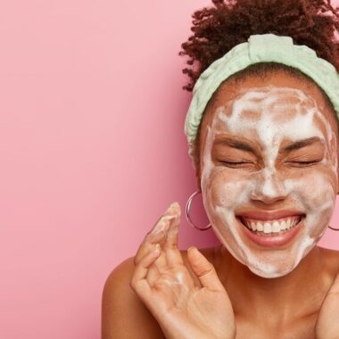 Mulher negra feliz com máscara de skincare no rosto