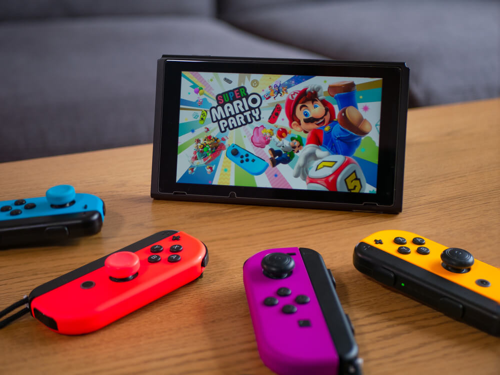 Mario Party iniciando em um Nintendo Switch. Ao redor, quatro controles coloridos.