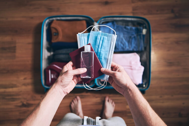 viagem na pandemia: pessoa colocando máscara e álcool em gel na mala 