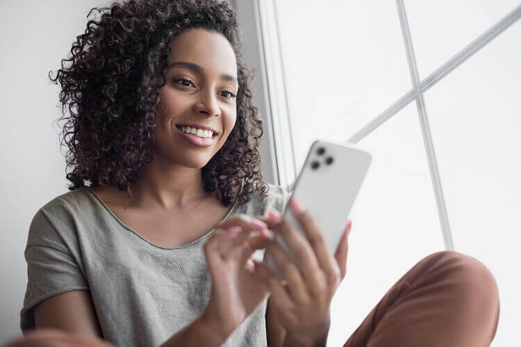 Mulher negra mexendo em celular sentada