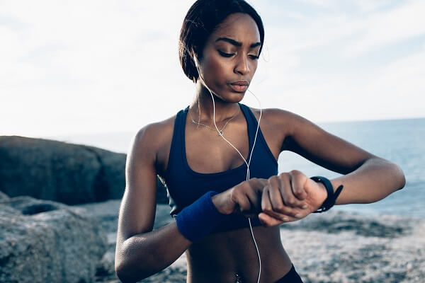 corredora ao ar livre com fone de ouvido e relógio gps. mulher veste um top preto e está com cabelo amarrado.